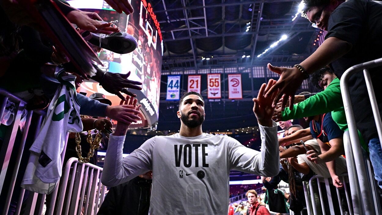 Jayson Tatum walks through an NBA arena tunnel, high-fiving fans on both sides while wearing a white “VOTE” shirt.