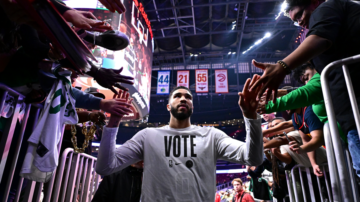 Jayson Tatum walks through an NBA arena tunnel, high-fiving fans on both sides while wearing a white “VOTE” shirt.
