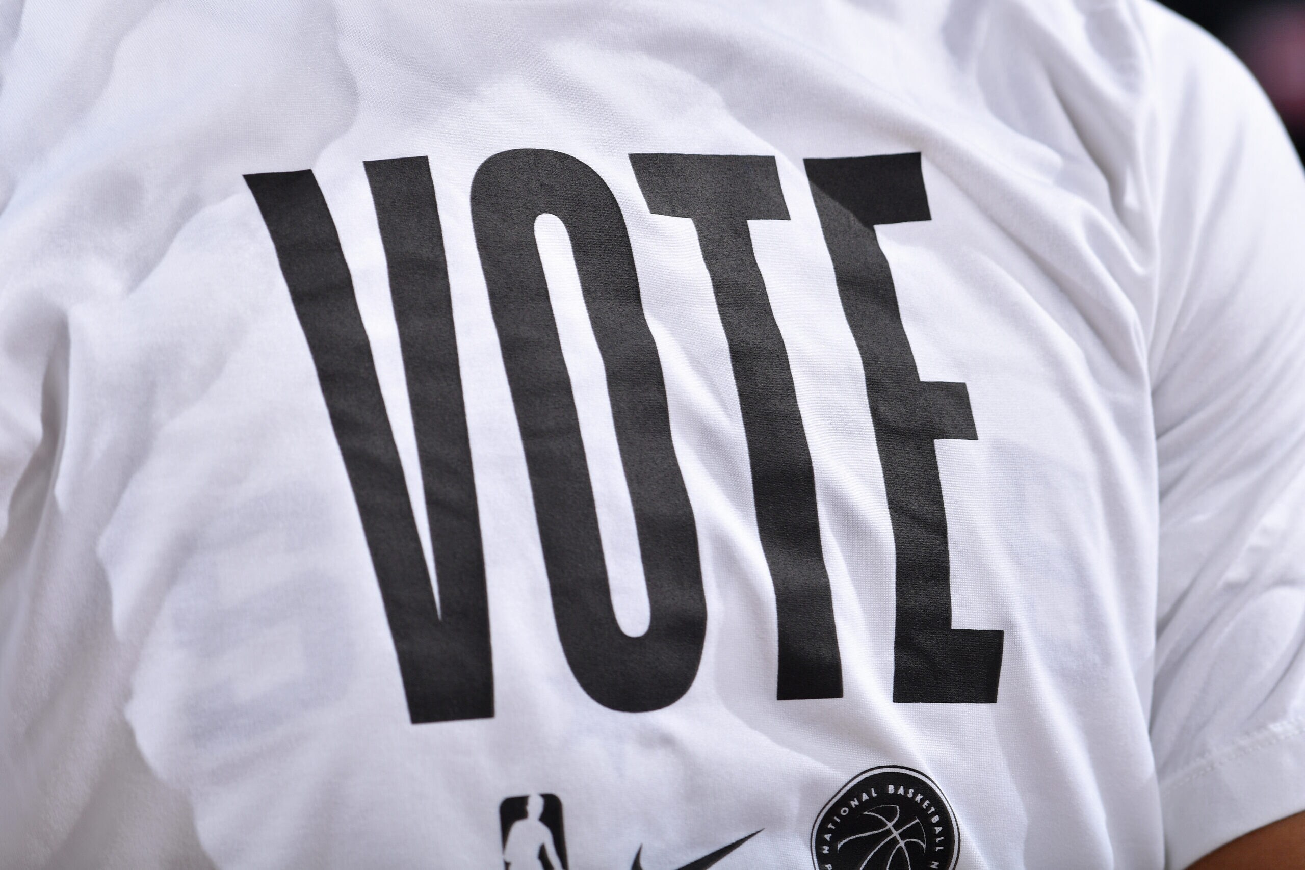 Close-up of an NBA-branded white T-shirt with “VOTE” printed in large black letters.