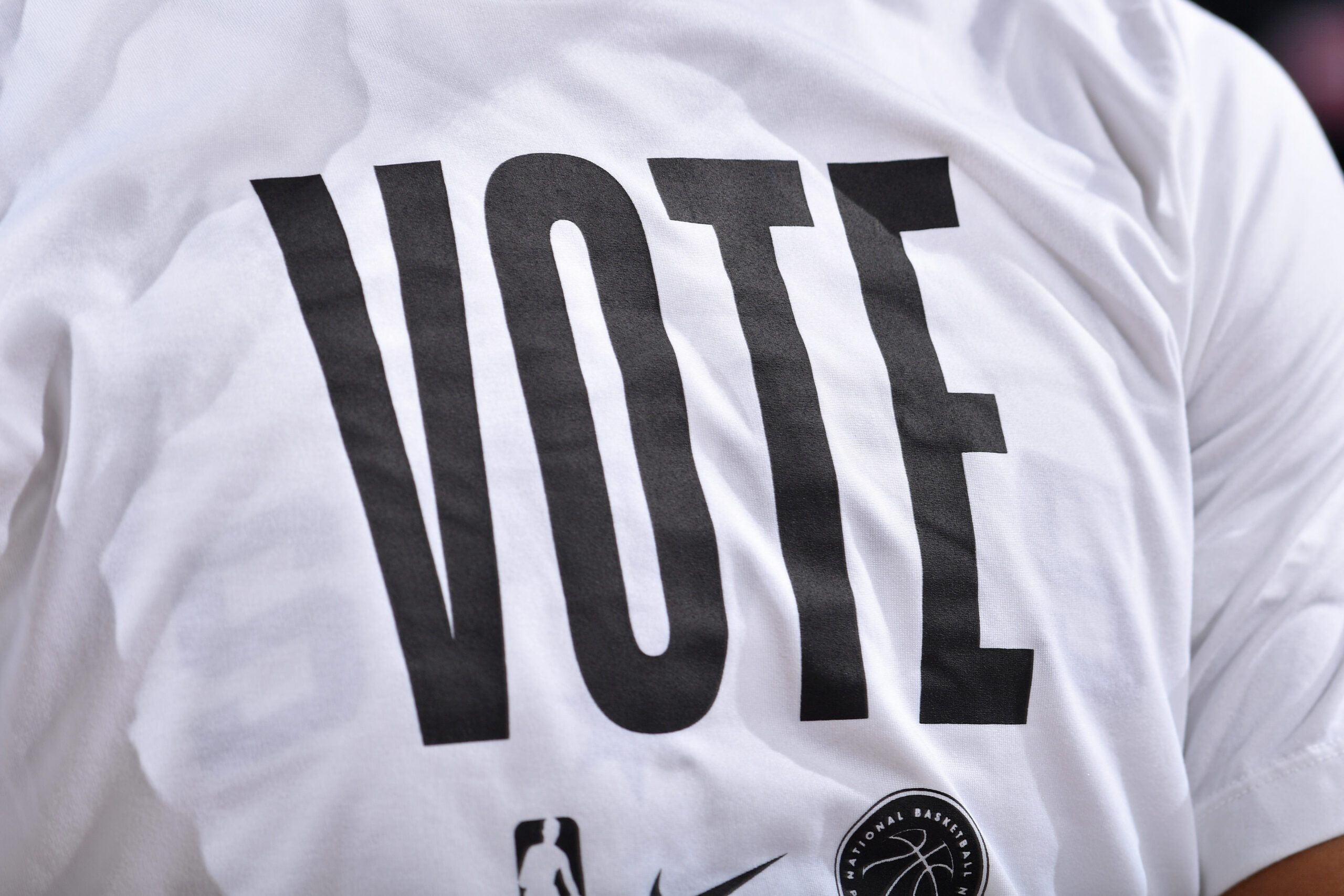 Close-up of an NBA-branded white T-shirt with “VOTE” printed in large black letters.